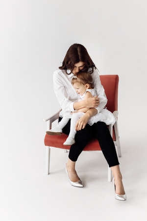 A beautiful young mother holds her adorable daughter in her arms, hugging her. Mom gently kissing and looking at her baby. Happy motherhood concept. Photo in the studio. High quality photoの写真素材