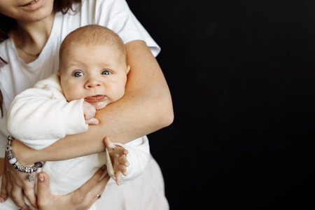 A young mother lovingly holds the baby in her arms, enjoying the moment. Baby cute posing for a...