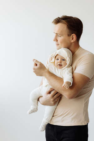 Happy young dad is photographed with his little daughter in the studio. Caring dad holds the baby in...