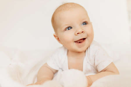 Portrait of wonderful baby girl laying on comfortable bed at home, adorable cute toddler look around with big interest, smiling, childhood and childcare concept. High quality photoの写真素材