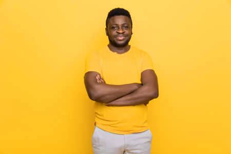 Portrait of young attractive candid afro american male looking at camera, hands crossed, wearing modern yellow outfit isolated over bright color yellow background. High quality photoの写真素材