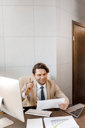 Thoughtful millennial male closes eyes and puts finger up thinking of creative idea sitting with pc...