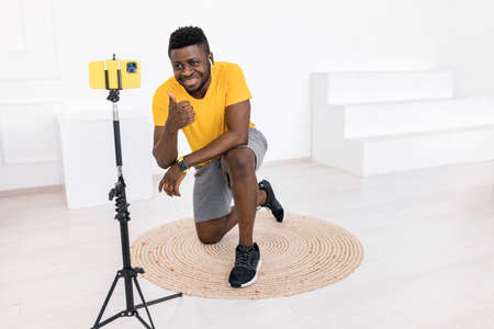 Handsome young male is sitting in front of the smartphone camera, making video lesson about sport...