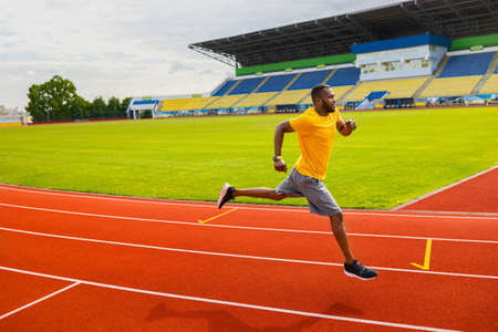 Professional focused afro american athlete runner training running on racetrack at stadium. Side view of black male runner sprinter running on the sport track, preparing for championship.の写真素材