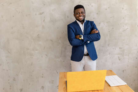 Portrait of smart afro american man businessman leader staying near desk and yellow laptop, smiling...