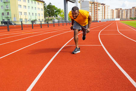 Front view of young afro american male sprinter in yellow sportswear running on the sport track....