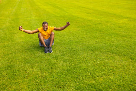 Exited young african american sportsman athlete in bright yellow sportswear, sitting on grass, smiling celebrating success, victory. Healthy lifestyle concept. Copy space. High quality photoの写真素材
