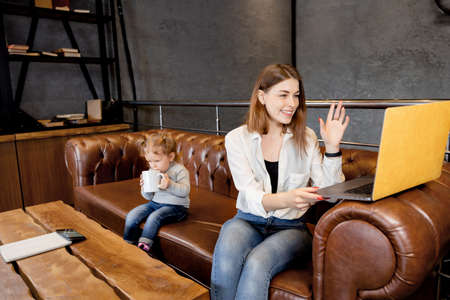 Young happy business woman in maternity leave using laptop, waving hello to colleagues on video...