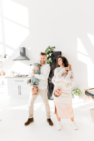 Joyful beautiful parents having fun with little kids, holding them upside down, smiling. Charming father with lovely mother playing at home with small children, laughing, happy family leisure conceptの写真素材