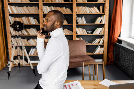 Happy male employee or student is having a phone conversation with friend or colleague, smiling. Joyful young adult businessman is sitting at the work desk in home office, communication concept. high quality photoの写真素材