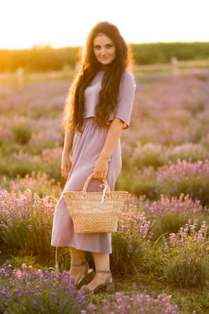 Happy portrait of stylish gorgeous female walking at the field, posing, looking at the camera. Brunette woman with picnic basket spending weekends outdoors, beautiful nature concept.の写真素材
