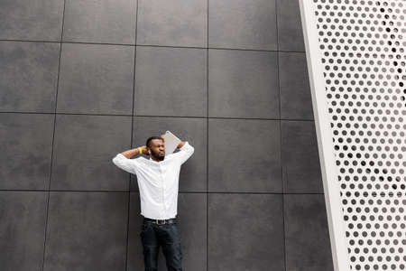 Relaxed young adult businessman is standing outdoors in white shirt, looking at the side. Stylish...