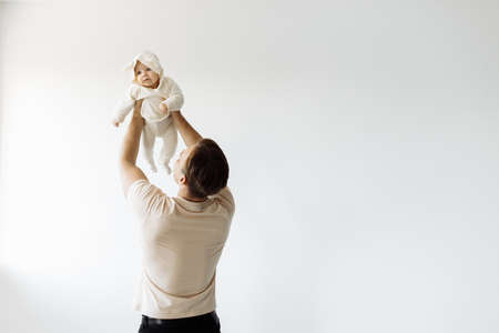 Happy dad holds the baby in his arms, lifting her up. The adorable little daughter is overjoyed. Play together in a room on a white background. family concept. high quality photoの写真素材