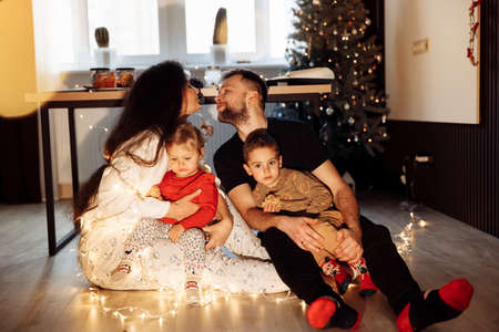 Overjoyed parents with little kids sitting at home, smiling and cuddling. Happy family with adorable...