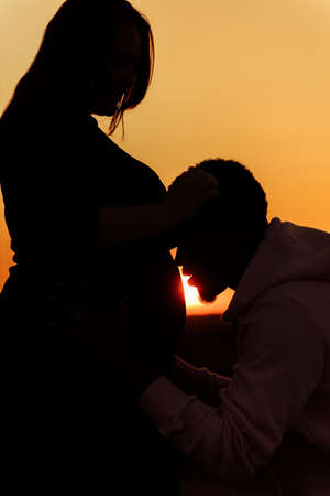 Silhouettes of lovely couple, handsome man kiss beautiful woman at sunset, enjoy tender moments, caring husband and loving wife spend time together, weekends outdoors concept. high quality photoの写真素材