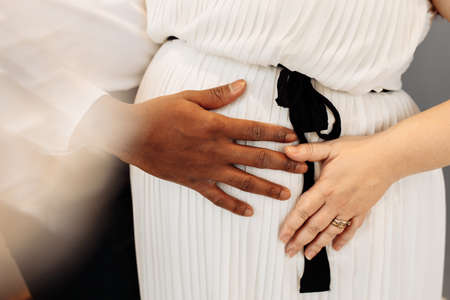 Close up charming African American man hug pregnant belly of beautiful white woman, happy couple expect for a baby, excited about parenting, motherhood and fatherhood concept. high quality photoの写真素材