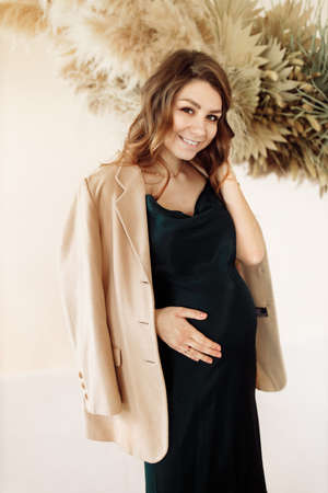 Gorgeous pregnant woman sit on the chair in studio, posing, wearing green dress, expect for a first...