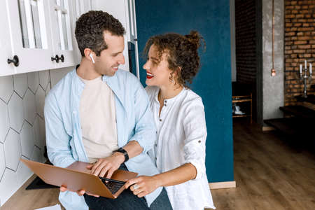 Happy family couple are standing at the kitchen at home, doing online shopping or chatting with...