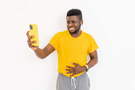Smiling Afro American student or freelancer standing near the wall in trendy yellow t-shirt, having...