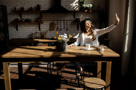 Young beautiful girl doing selfie on the kitchen at sunny weather . high quality photoの写真素材