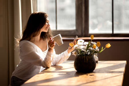 Young woman with cup of coffee is stare at the phone at kitchen . high quality photo