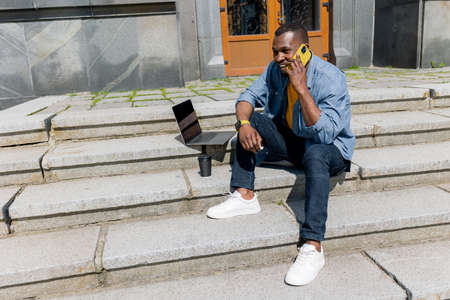 Young attractive african american freelancer businessman or student sitting on stairs in urban area...