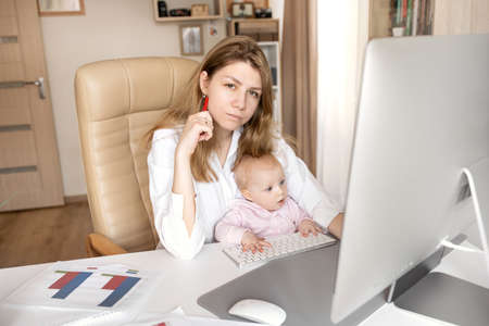 Lovely young single mother and little infant toddler daughter using computer online apps, making video call, having fun, mommy teaching little girl to use computer, watching cartoons togetherの写真素材