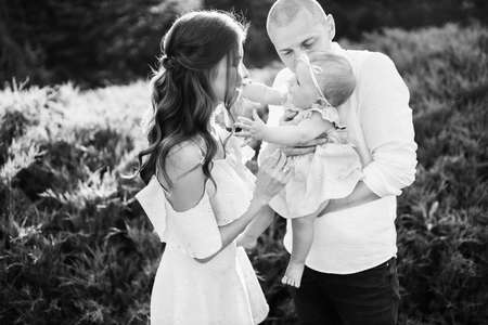 Little cute baby girl with mom and dad, beautiful daughter sitting on strong fathers arms and smile...