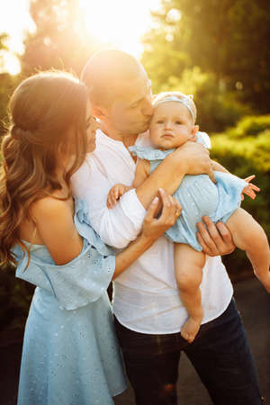 Portrait of young family at the park, lovely father hold cute toddler in arms, beautiful wife hugging caring husband, smiling, dad kissing little daughter, parenting concept. high quality photoの写真素材
