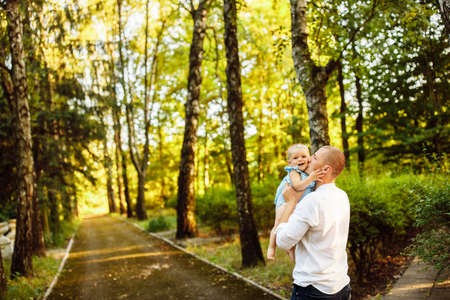 Handsome man hold in arms beautiful baby girl at the park, young father kissing little daughter, hugging, cute toddler smiling, enjoy tender family moments, parenthood concept. high quality photoの写真素材