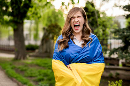Screaming girl standing in Ukrainian flag worried about war. Young woman is feeling emotional pain after reading the news. Freedom and patriot of Ukraine.. Pray for Ukraine. stop war. blue yellow.の写真素材