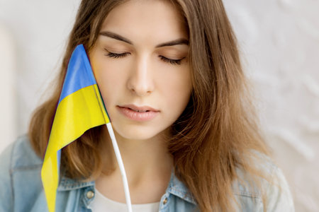 Independent serious girl holds the Ukrainian flag and close eyes. Patriot of her country. Pray for Ukraine. Fight for freedom. stop war. blue yellow. high quality photoの写真素材