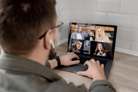 Back view of male employee having an online conference with colleagues, using a laptop. Young businessman discussing corporate project with coworkers by video call, internet meeting conceptの写真素材
