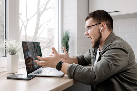 Surprised male freelancer holding a video conference, surprised with a new decision about a project, the results of working with his colleagues.The indignant guy is working on the bugs via video linkの写真素材