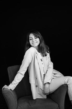 Black and white portrait of a happy business woman sitting in a studio in a chair. Posing for the camera with closed eyes.A young girl with a wide smile, being photographed against a black background.の写真素材