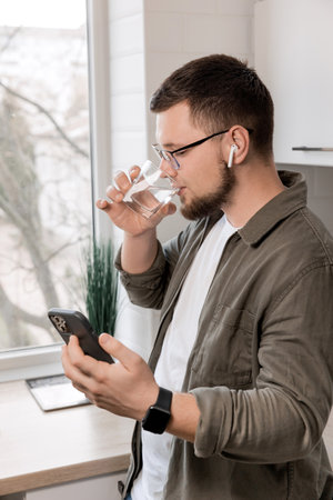 A young guy communicates with his family on the phone via video communication and drinks water. Work at home during the war in Ukraine. Health and peace concept.の写真素材