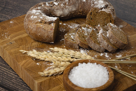 Bread and wheat on a cutting board with salt on wooden background