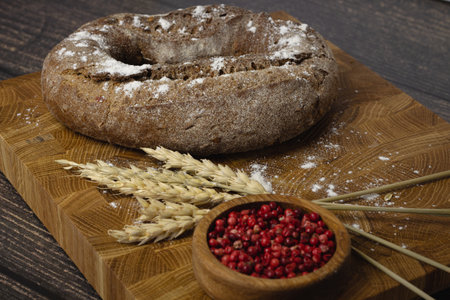 Rye bread on a wooden cutting board with ears of wheat and red pepper