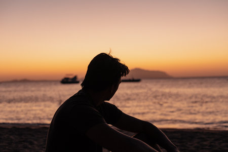 Silhouette of a man sitting on the beach and watching the sunset