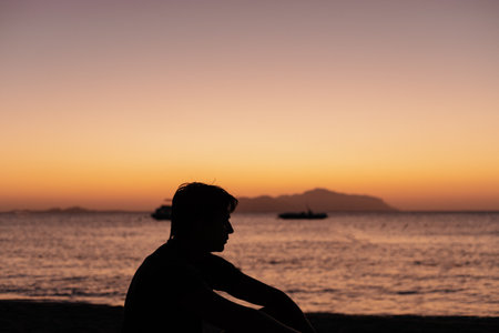 Silhouette of a man sitting on the beach at sunset.