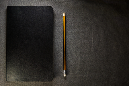 Top view of closed black cover notebook with pencil on gray background.の写真素材