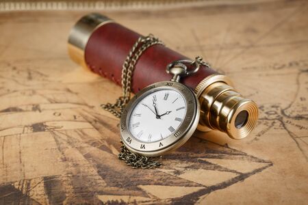 A spyglass and a pocket watch lying on an old mapの写真素材