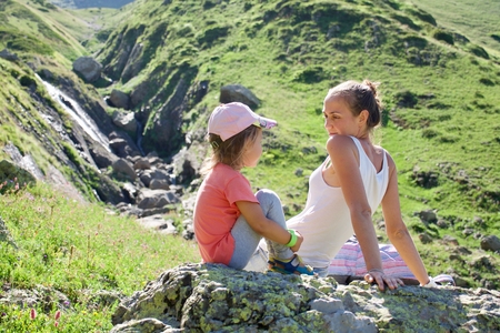 Young mother and cute little daughter resting on the big stone at travel excursion at summer vacation.の写真素材