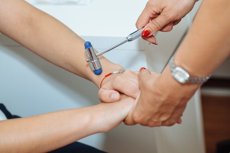 Cropped image of neurologist testing reflex on a female patient using a hammer