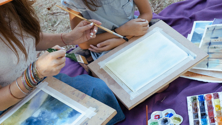 A lesson in drawing of watercolor paints for young girl on the nature at park. Crop shot of teaching process.の写真素材