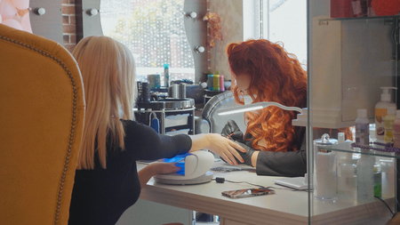 Manicurist makes a procedure of painting nails her blond female client in red color. Manicure procedure in the beauty salonの写真素材