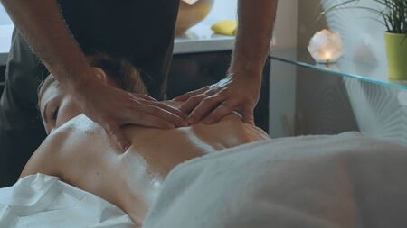 Male massagists hands massaging attractive ladys back. Beautiful young woman is lying on the couch at luxury spa salon and getting a massage.の写真素材