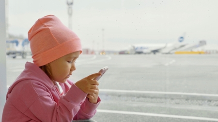 Cute little girl using smart phone in airport, close-up.の写真素材