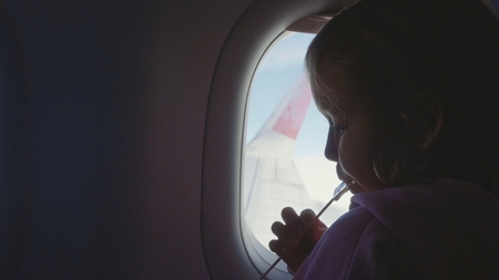 Silhouette child girl sucking sweets on wooden stick over porthole in airplane
