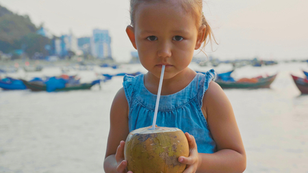 Little girl drinks coconut water at seafront on sunset.の写真素材